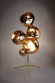 Tom Dixon Standkronleuchter MELT in Gold auf grauem Hintergrund, stimmungsvolle Beleuchtung, ideal für festliche Dekorationen.